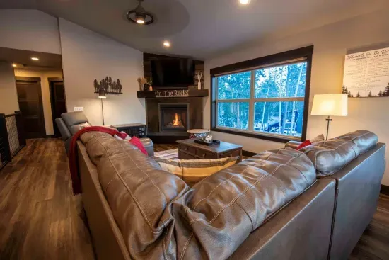 Visualize lounging in the expansive living space at "On The Rocks," where the cozy fireplace flickers warmly beside a large TV. 