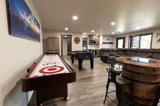 Spacious lower-level game room featuring shuffleboard, foosball, pub seating, and a cozy lounge area for movie nights and friendly competition.