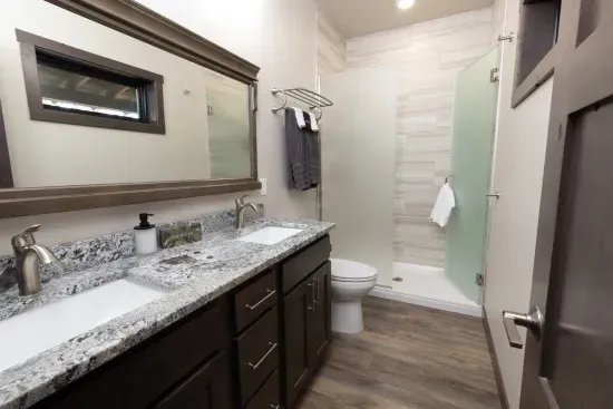 Private ensuite bathroom for the main-level king suite featuring double sinks, granite counters, and a spacious walk-in shower. A comfortable and convenient setup for guests staying on the main floor.