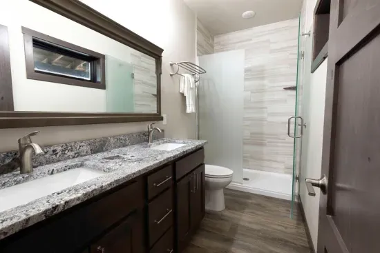 Private ensuite bathroom for the main-level king suite featuring double sinks, granite counters, and a spacious walk-in shower. A comfortable and convenient setup for guests staying on the main floor.