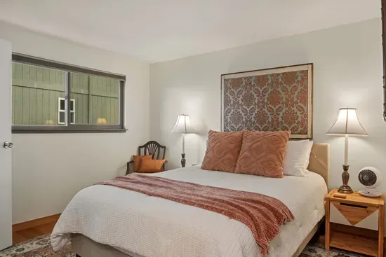 2nd bedroom with Queen Bear hybrid mattress with block out blinds, bedside tables with reading lamps and a rotating fan.