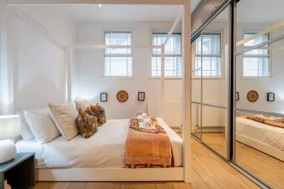 A white four-poster bed in crisp linen, mirrored wardrobes and vintage teak — a calm, light-filled retreat after a night in Soho.