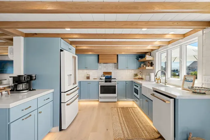 Bright coastal kitchen with blue cabinets, big windows, and warm wood beams