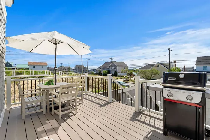 Sunny private deck with outdoor dining, umbrella shade, and gas grill