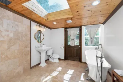 Spa-like bathroom featuring a classic claw-foot tub, skylight, elegant pedestal sink, and abundant natural light.