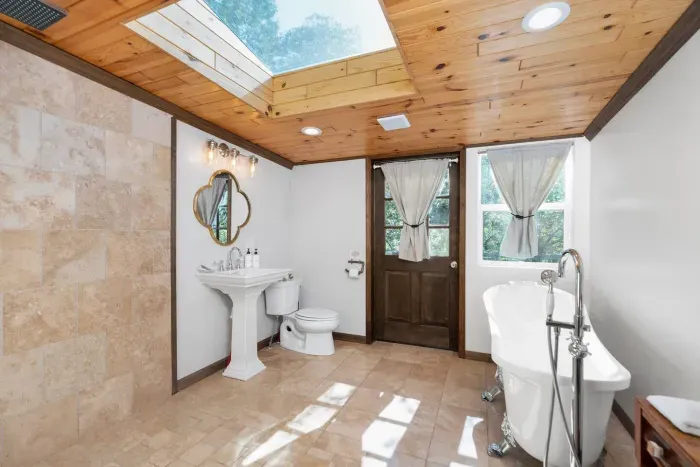 Spa-like bathroom featuring a classic claw-foot tub, skylight, elegant pedestal sink, and abundant natural light.