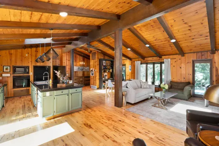 Spacious Open-Concept Living Area: Bright, inviting great room with comfortable seating, a fully equipped kitchen, warm wood interiors, and large windows overlooking the surrounding greenery.