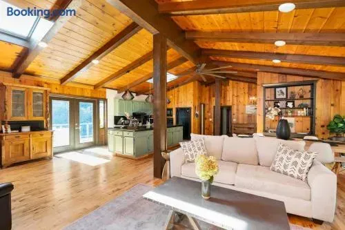 Spacious rustic cabin interior with warm wood-paneled walls and ceilings, exposed beams, skylights, a cozy living area with a neutral sofa, open kitchen, and abundant natural light.