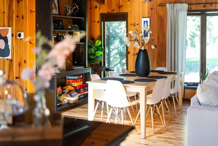 Bright dining area with seating for eight, surrounded by warm wood accents, natural light, and a collection of games for guests to enjoy.