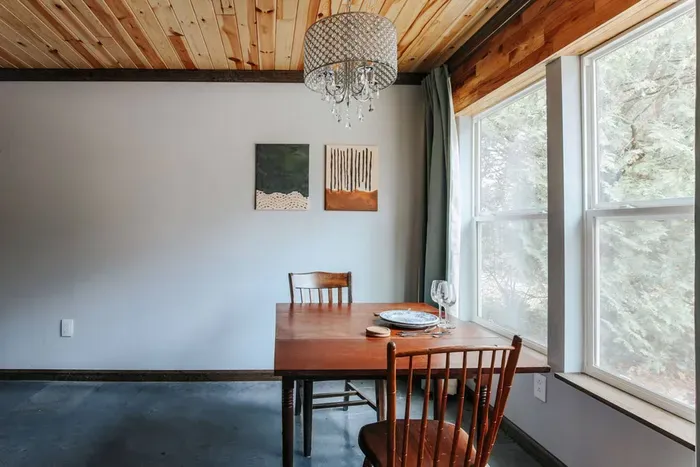 Inviting dining area with forest views, warm wood accents, and elegant chandelier lighting.