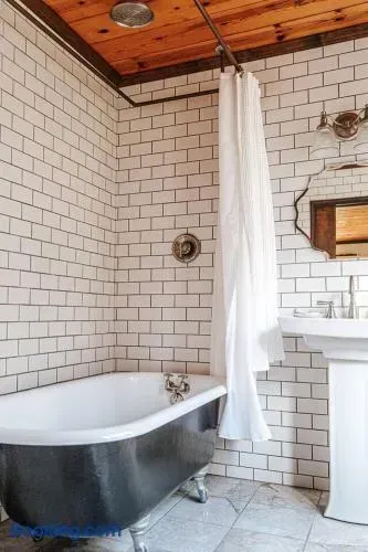 Rustic bathroom featuring a freestanding clawfoot tub, white subway-tile walls, warm wood-paneled ceiling, vintage-style fixtures, and a clean white pedestal sink.