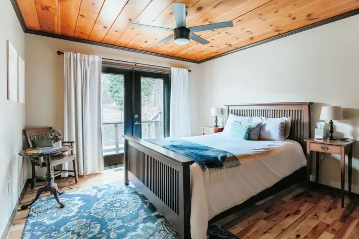 **Cozy Bedroom:** Comfortable king bed, private deck access, ceiling fan, and warm cabin-inspired décor.