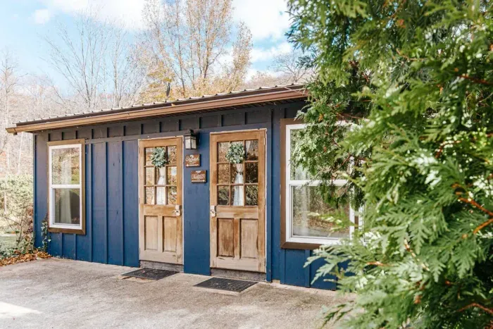 Charming blue Suites, surrounded by trees, with rustic wood doors and a peaceful woodland setting.