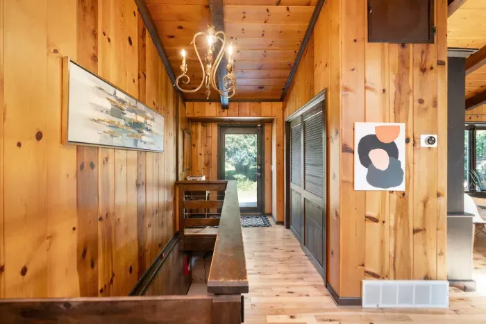 Welcoming Entryway: Warm wood-paneled hallway with rustic details, stylish artwork, and a charming chandelier leading into the main living spaces.