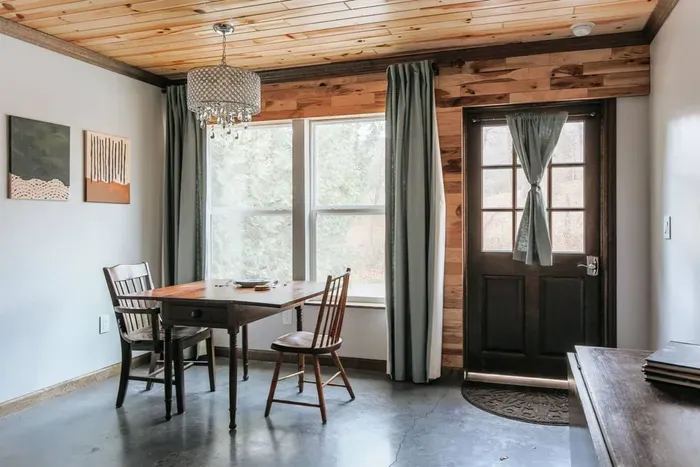 Cozy dining nook with forest views, rustic wood accents, and elegant chandelier lighting.