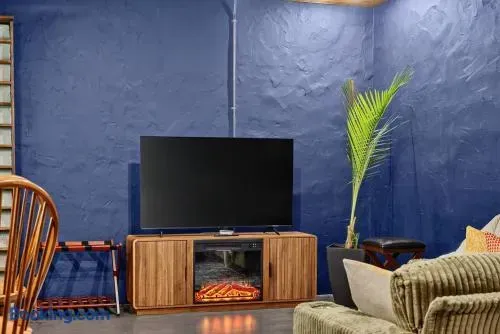 Cozy cabin living area with deep blue textured walls, a wall-mounted TV, warm wood media console, plush green seating, and a tropical plant adding a natural touch.