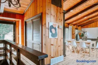 Warm, rustic cabin interior with natural wood walls and exposed beams, connecting a cozy upper landing to a bright dining area with modern white seating and minimalist décor.