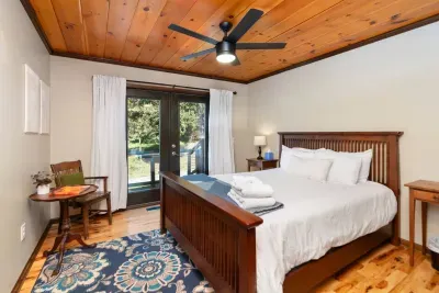 Serene Bedroom: Comfortable king-size bed with fresh linens, warm wood accents, a ceiling fan, and direct access to a private outdoor deck surrounded by nature.