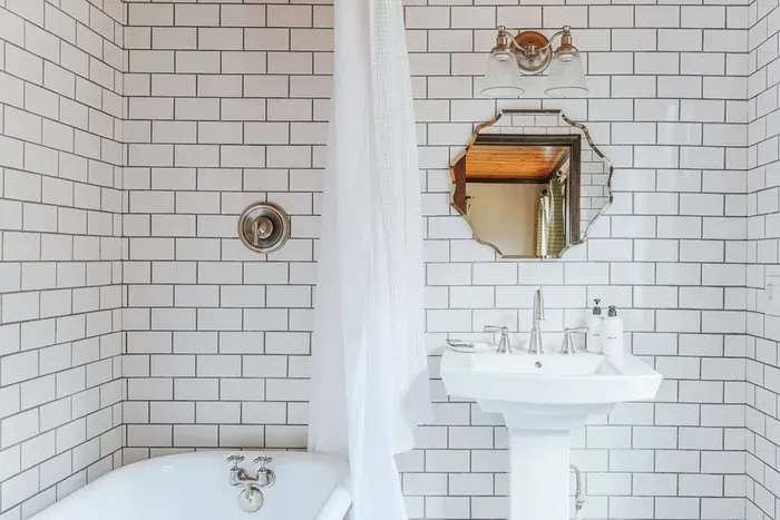 Bright bathroom with a classic bathtub, subway tile walls, pedestal sink, and decorative mirror.