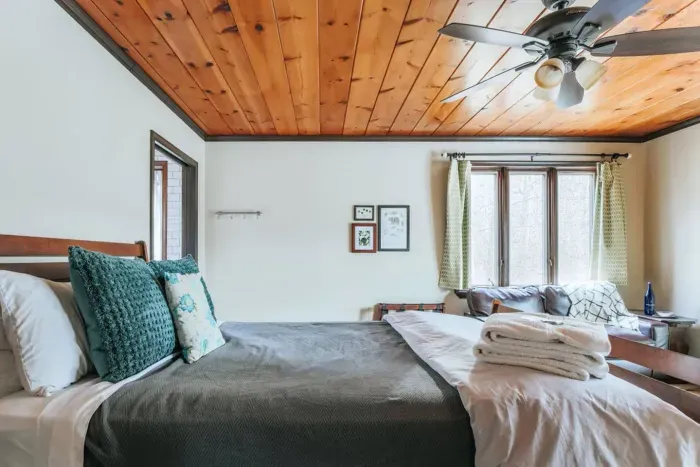 Cozy Cabin Bedroom: Comfortable king bed, warm wood ceiling, ceiling fan, and peaceful woodland views.