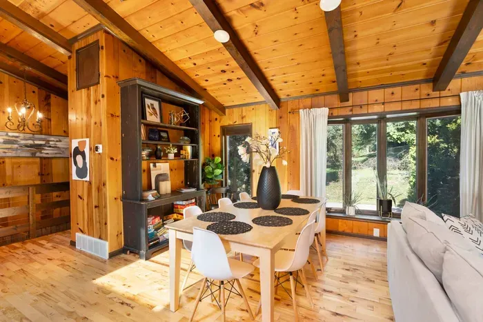 Dining Area: Bright dining space with seating for the group, surrounded by warm wood accents, large windows, and peaceful wooded views.