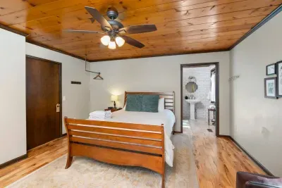 Cozy Bedroom: Comfortable bed with fresh linens, warm wood accents, ceiling fan, and direct access to the bright, well-appointed bathroom.