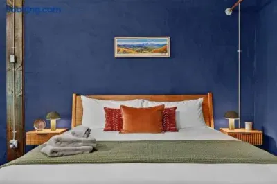 Inviting cabin bedroom with rich blue walls, a warm wood bed frame, crisp white linens, rust-colored accent pillows, and soft green bedding, creating a cozy and stylish retreat.