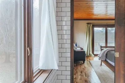 Bright bathroom with a window overlooking the bedroom, featuring natural light and wood accents.