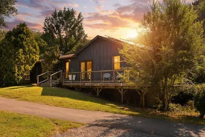 Charming mountain retreat glowing at sunset, with a spacious deck and peaceful wooded surroundings.