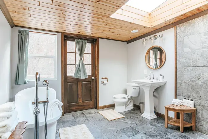 Bright, spa-like bathroom with a claw-foot tub, skylight, slate tile, and elegant pedestal sink.