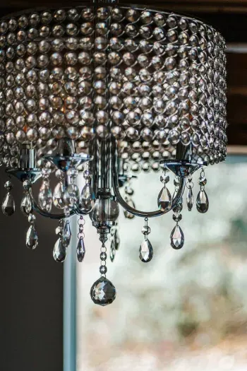 Close-up of an elegant crystal chandelier with cascading faceted drops, sparkling beautifully against a softly blurred woodland view.