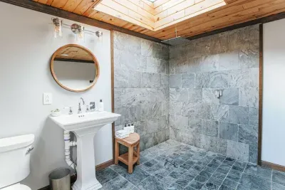 Spa-like bathroom with a spacious slate-tile walk-in shower, skylight, and elegant pedestal sink.