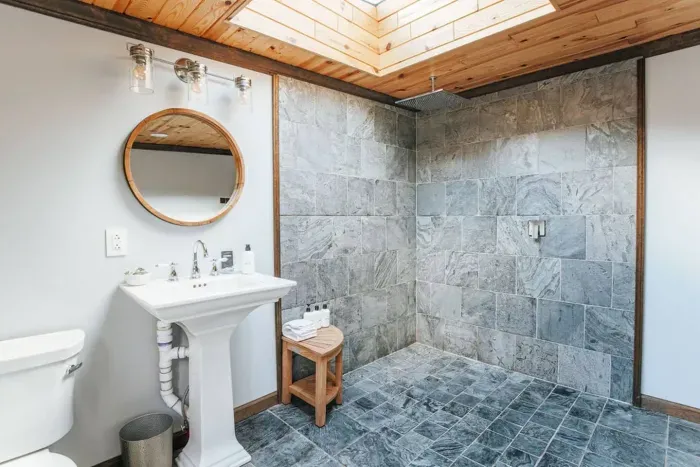 Spa-like bathroom with a spacious slate-tile walk-in shower, skylight, and elegant pedestal sink.