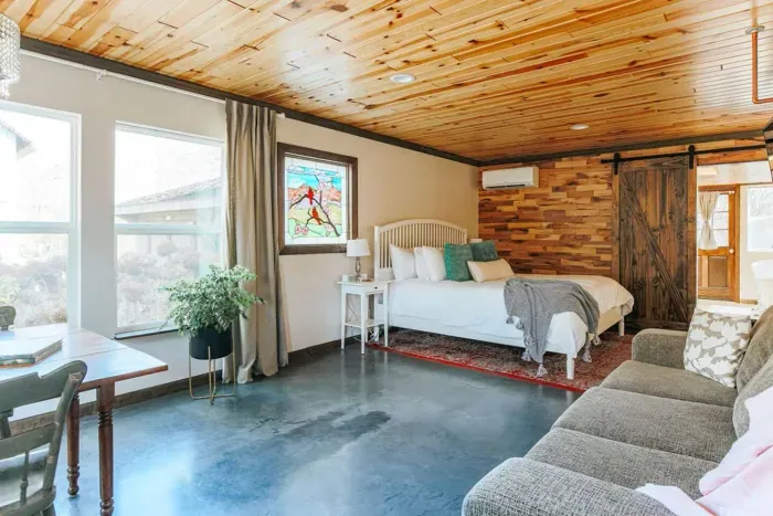 Bright, spacious suite with a comfortable queen bed, cozy sofa, dining area, and warm wood accents.
