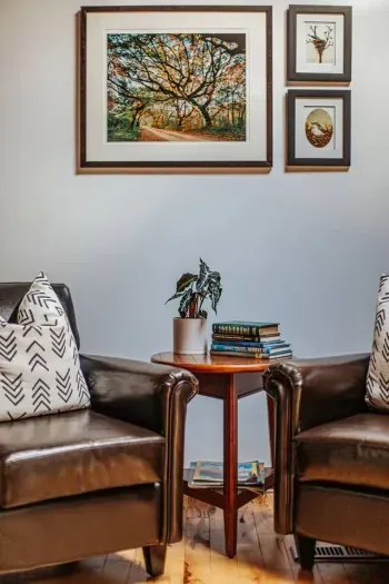 Cozy Sitting Area: Two leather armchairs with a charming side table, books, and nature-inspired artwork create a warm, inviting space to relax.