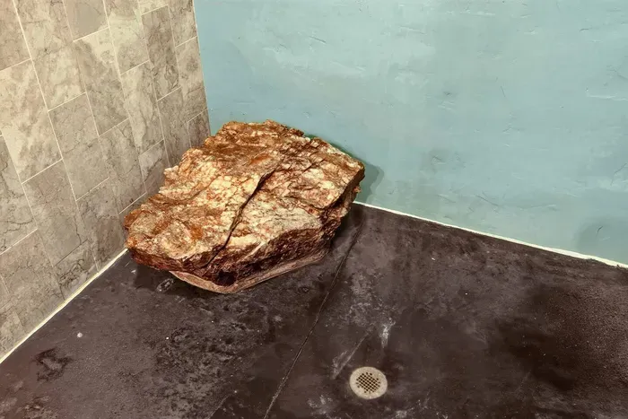 Walk-in shower with a natural stone bench, textured walls, and a floor drain.