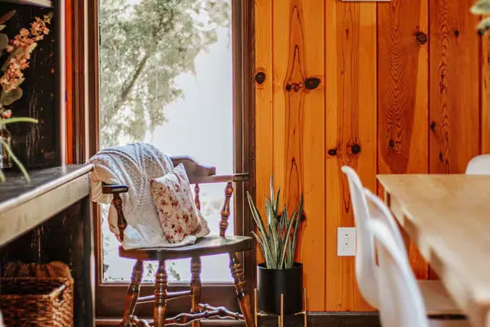 Cozy dining nook with a vintage chair, warm wood paneling, and peaceful woodland views.