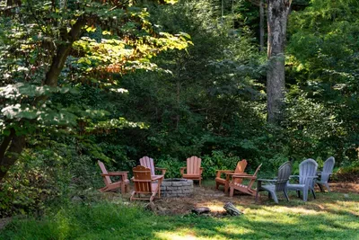 Secluded outdoor fire pit surrounded by comfortable Adirondack chairs and lush woodland.