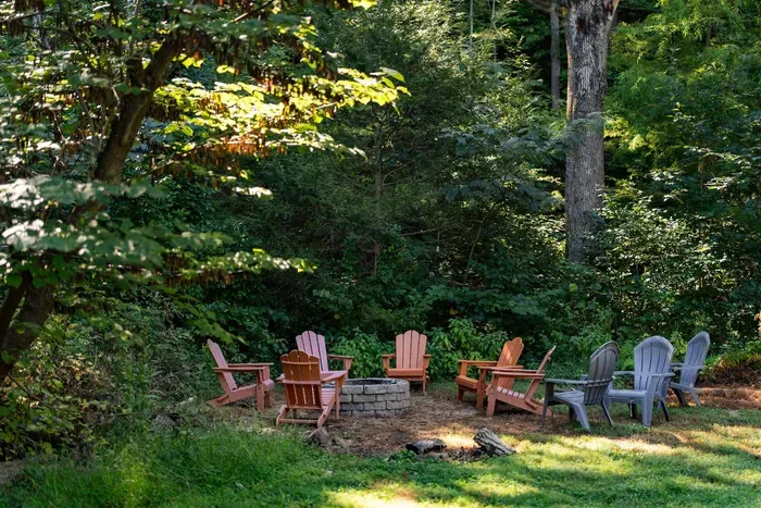 Secluded outdoor fire pit surrounded by comfortable Adirondack chairs and lush woodland.