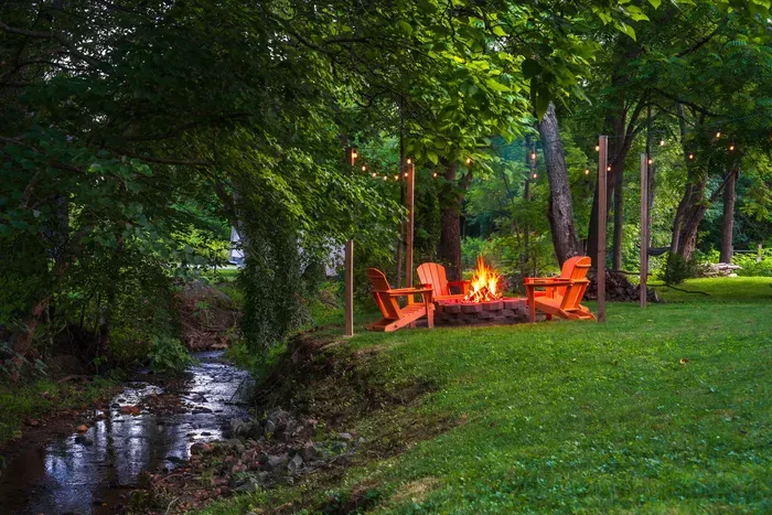 Creekside fire pit with Adirondack chairs under glowing string lights