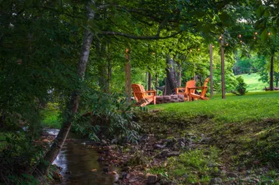 Creekside fire pit retreat with Adirondack chairs and glowing string lights