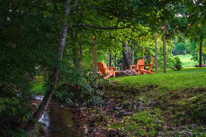 Creekside fire pit retreat with Adirondack chairs and glowing string lights