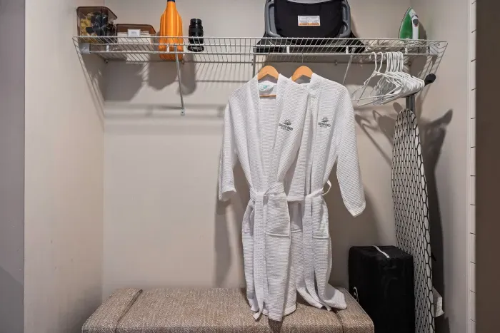Organized closet with robes, storage bench, iron, and extra hangers
