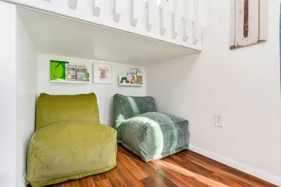 Discover a cozy reading nook tucked under the stairs, complete with plush seating and a selection of children's books.  Perfect for a quiet escape or storytime with the little ones.