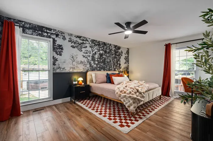 Stylish, sunlit bedroom with mural wall, cozy bed, and workspace