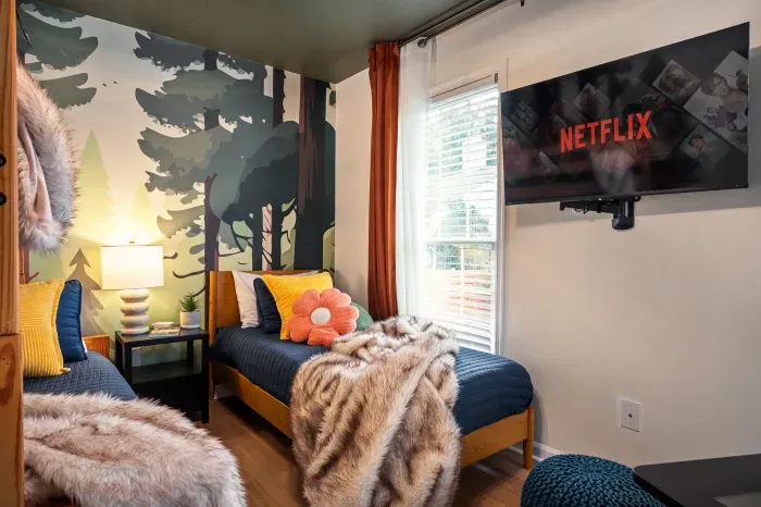 Cozy twin room with forest mural, streaming TV, and warm natural light