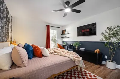 Cozy modern bedroom with plush bedding, TV, workspace, and natural light