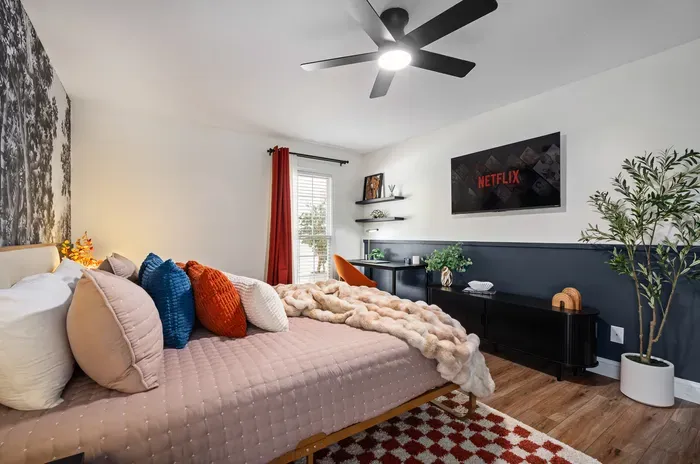 Cozy modern bedroom with plush bedding, TV, workspace, and natural light
