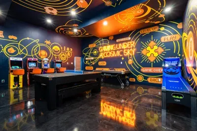 The game room wired for the long tournament night. Ping pong center stage, skee-ball glowing along the wall, the arcades ready, nobody going to bed at a reasonable hour.