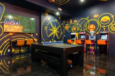 Game night anchor. Ping pong front and center, the arcade lineup waiting along the wall, the TV keeping the game on in the background. The room everyone ends up in.